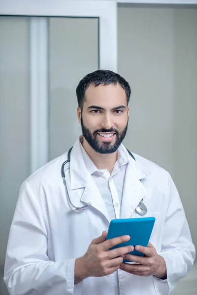 Medico maschio in vestaglia bianca che tiene una tavoletta e sorride — Foto Stock