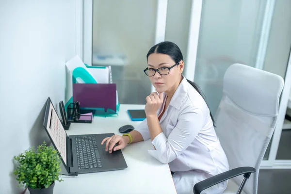 Female dark-haired doctor in eyewear looking thoughtful — Φωτογραφία Αρχείου