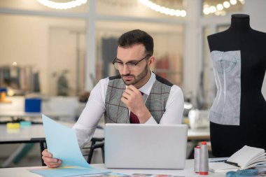 Male tailor sitting at laptop, propping chin on hand