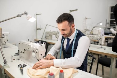 Male tailor sitting at sewing machine and sewing