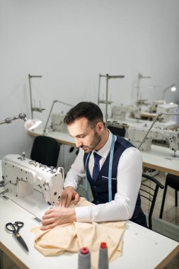 Male tailor sitting at sewing machine and sewing
