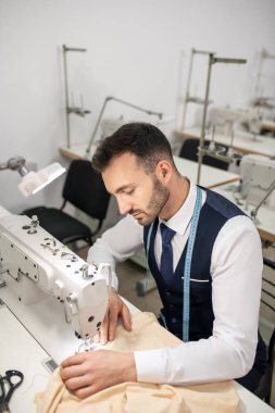 Male tailor sitting at sewing machine and sewing