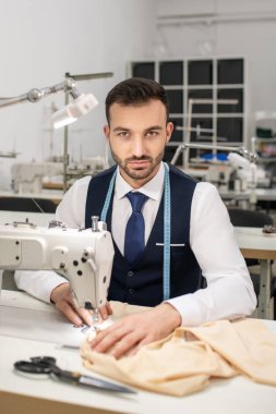 Male tailor sitting at sewing machine and sewing