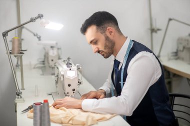 Erkek terzi dikiş makinesinde yarı yarıya oturuyor.