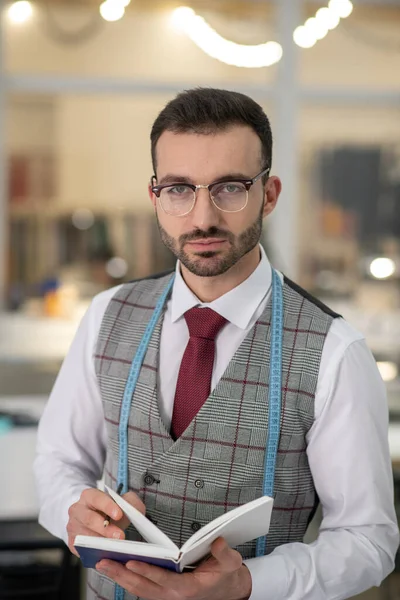 Male tailor standing, wearing glasses, holding notebook — ストック写真