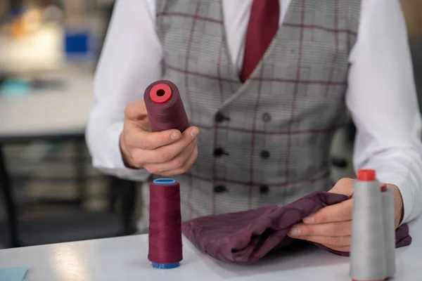 Hands of male tailor holding cloth and spool — Stock fotografie