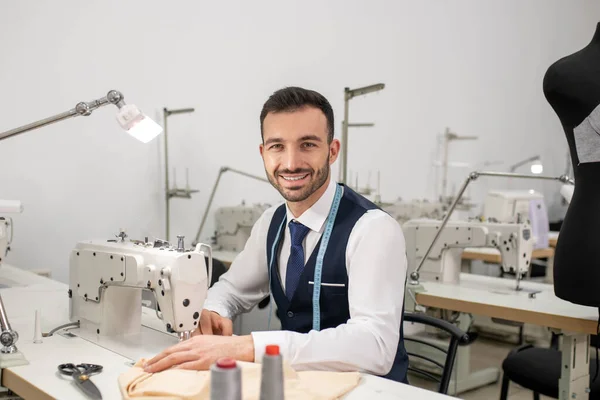 Sastre masculino sentado en la máquina de coser, sonriendo — Foto de Stock