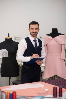 Male tailor standing next to dummy and making notes