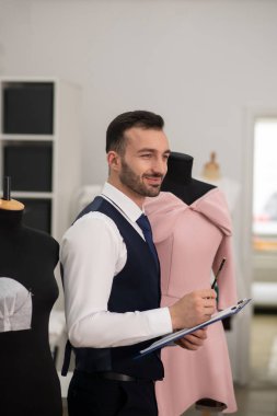Male tailor in a black vest smiling, thinking, making notes