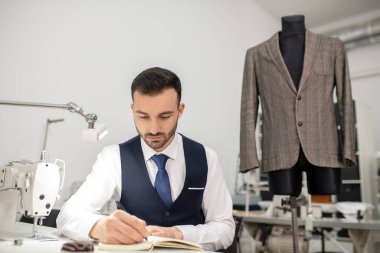Male tailor sitting at sewing machine, making notes