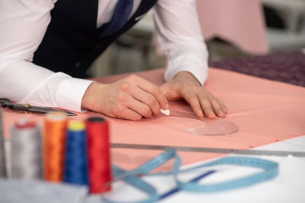 Hands of male tailor outlining pattern on pink cloth