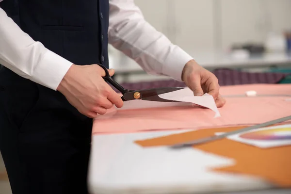 Mãos de alfaiate masculino cortando padrão de papel — Fotografia de Stock