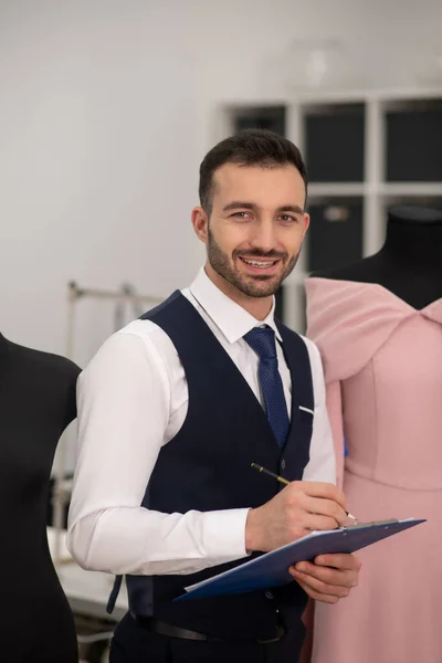 Male tailor standing next to dummy, smiling, making notes — Stock Fotó