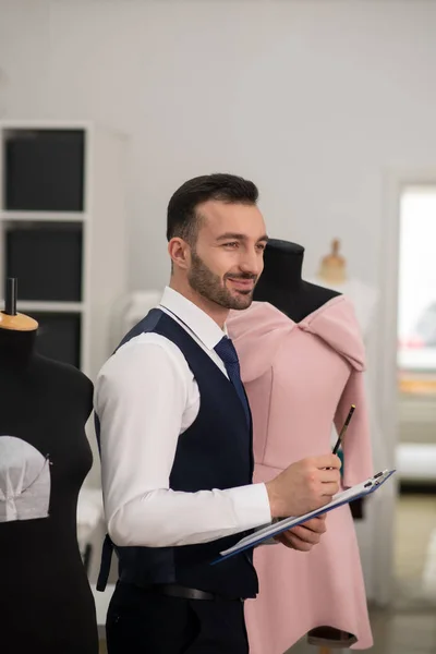 Male tailor in a black vest smiling, thinking, making notes — Stock Fotó