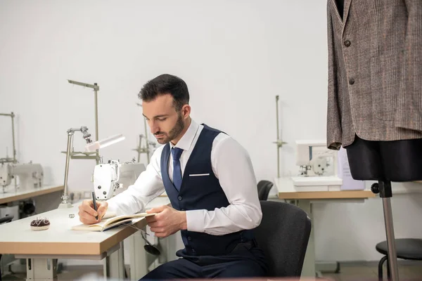 Sastre masculino sentado concentrado y tomando notas — Foto de Stock