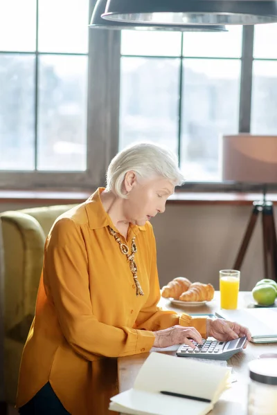 Grey-haired good-looking woman sitting at the table and looking concentrated