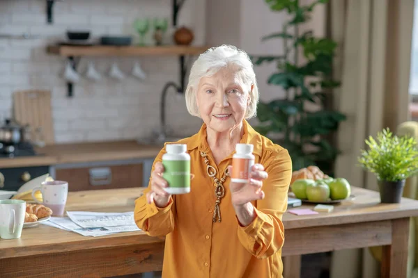 Mujer guapa de pelo gris mostrando dos frascos con vitaminas — Foto de Stock