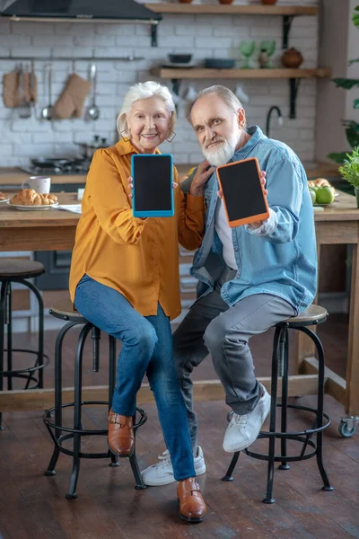 Alegre pareja de personas mayores mostrando sus nuevas tabletas — Foto de Stock