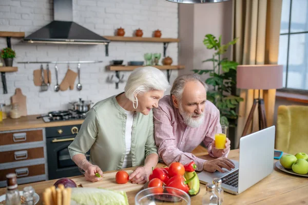 Pareja de seniors usando internet mientras preparan una cena — Foto de Stock