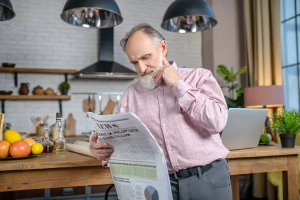 Figyelmes idős ember újságot olvas a konyhában. — Stock Fotó