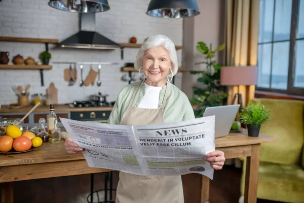 Улыбающаяся пожилая женщина читает большую газету — стоковое фото