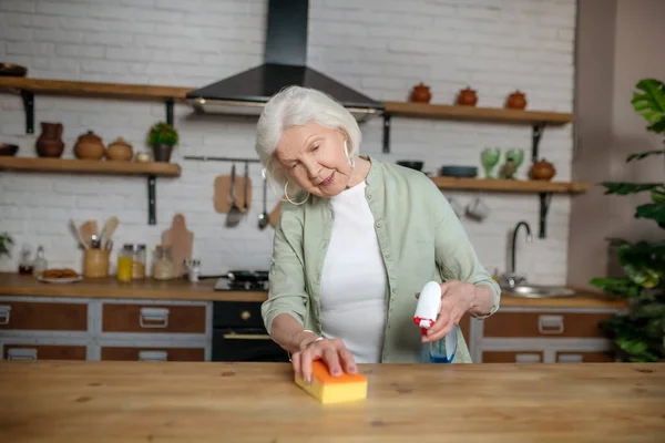 Starší žena uklízí stůl ve své kuchyni — Stock fotografie