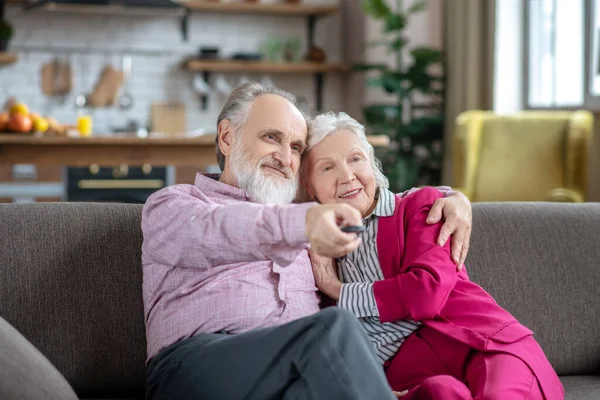 Man in a pink shirt hugging his wife while turning on tv — Zdjęcie stockowe