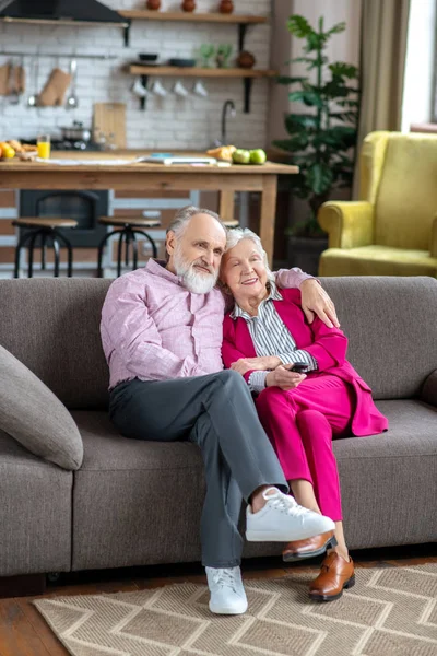 Homem de camisa rosa abraçando sua esposa enquanto assiste tv — Fotografia de Stock