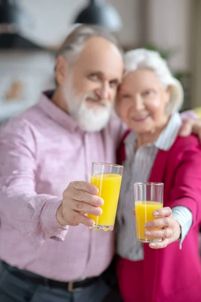 Casado casal sênior mostrando óculos com suco de laranja — Fotografia de Stock