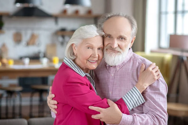 Mulher de cabelos grisalhos abraçando seu marido e olhando tranquilo — Fotografia de Stock