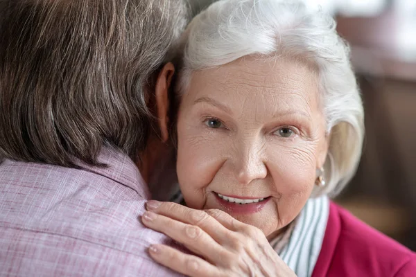 Grey-haired woman hugging her husband and looking happy — Stock Photo, Image