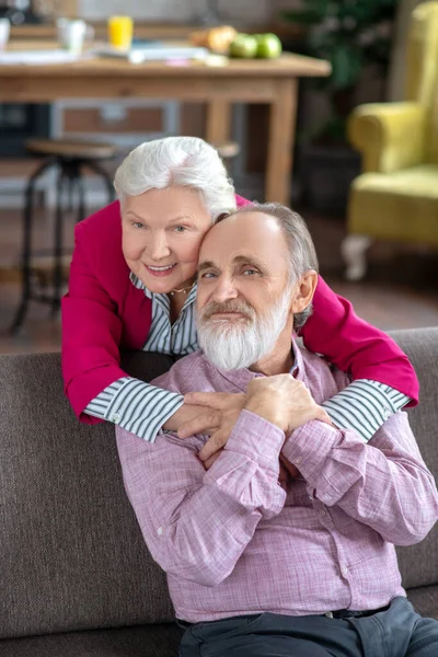 Mujer de pelo gris bien parecido abrazando a su marido y sonriendo — Foto de Stock