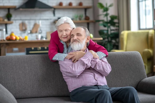 Good-looking grey-haired woman hugging her husband tight — Zdjęcie stockowe