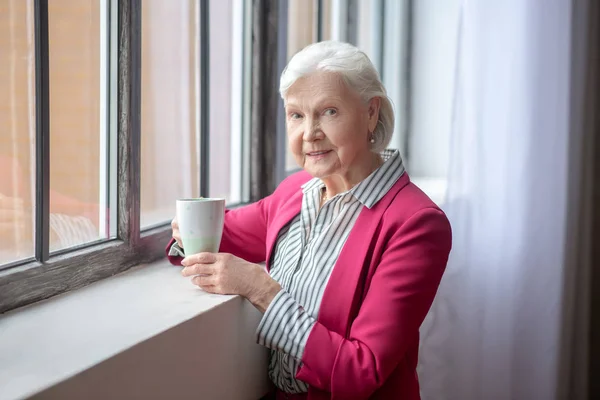 Grey-haired smiling lady standing at the window — Stockfoto