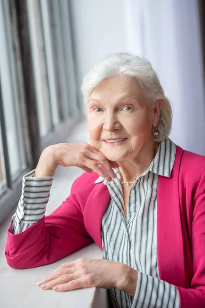 Grey-haired smiling lady standing near the window — Stockfoto