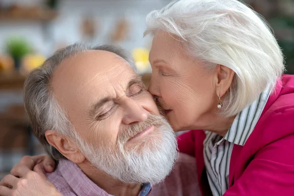 Старая седовласая женщина целует своего счастливого бородатого мужа — стоковое фото