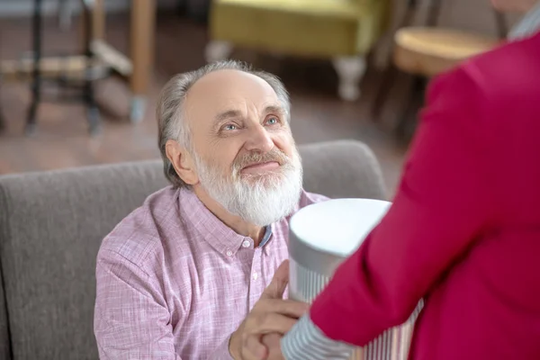 Grey-haired bearded man looking happy taking a gift from his wife — Stok fotoğraf