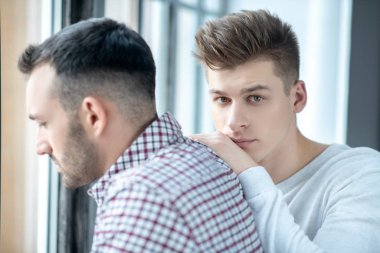 Two young men standing near the window feeling upset