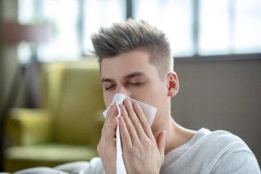 Fair-haired young man looking sick and sneezing
