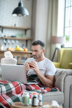 Dark-haired young man laying on the sofa feeling sick