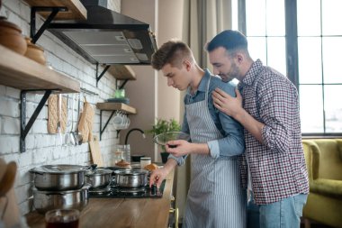 Two young men standing by the hob in the kitchen.
