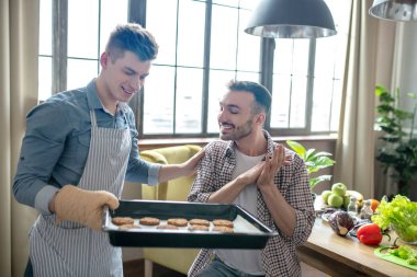 Man with a baking sheet showing pastries to a seated person.