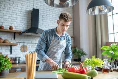 Young man in wireless headphones slicing fresh vegetables.