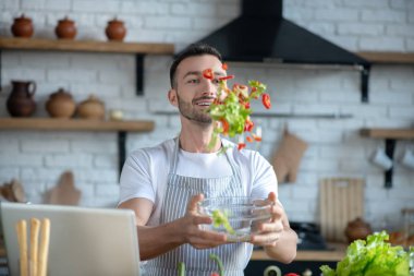 Young man mixing pieces of chopped vegetables tossing them up.