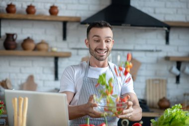 Dark-haired man with a bowl in his hands tossing chopped vegetables.
