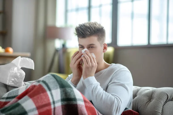 Fair-haired young man laying on the sofa and sneezing — Stock Photo, Image