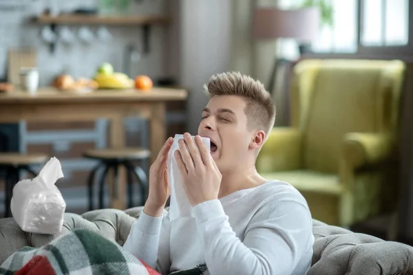 Fair-haired young man holding a napkin and sneezing — 图库照片