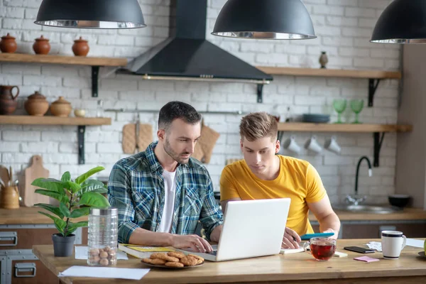 Two young men sitting in the kitching watching video tutorial — Stockfoto