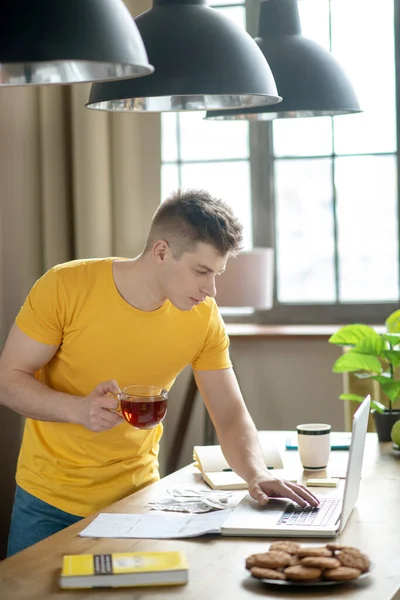 Young fair-haired man in yellow tshirt checking emails — 图库照片