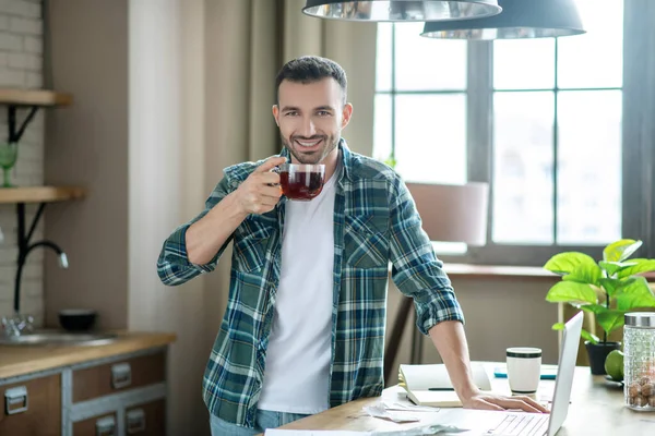 Young man in a checkered shirt standing near the table and having tea — Stockfoto